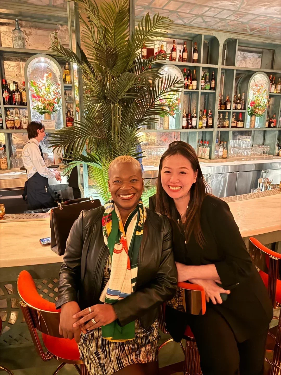 Two women smiling at Mawa's Kitchen in Aspen, with stylish bar and decor.